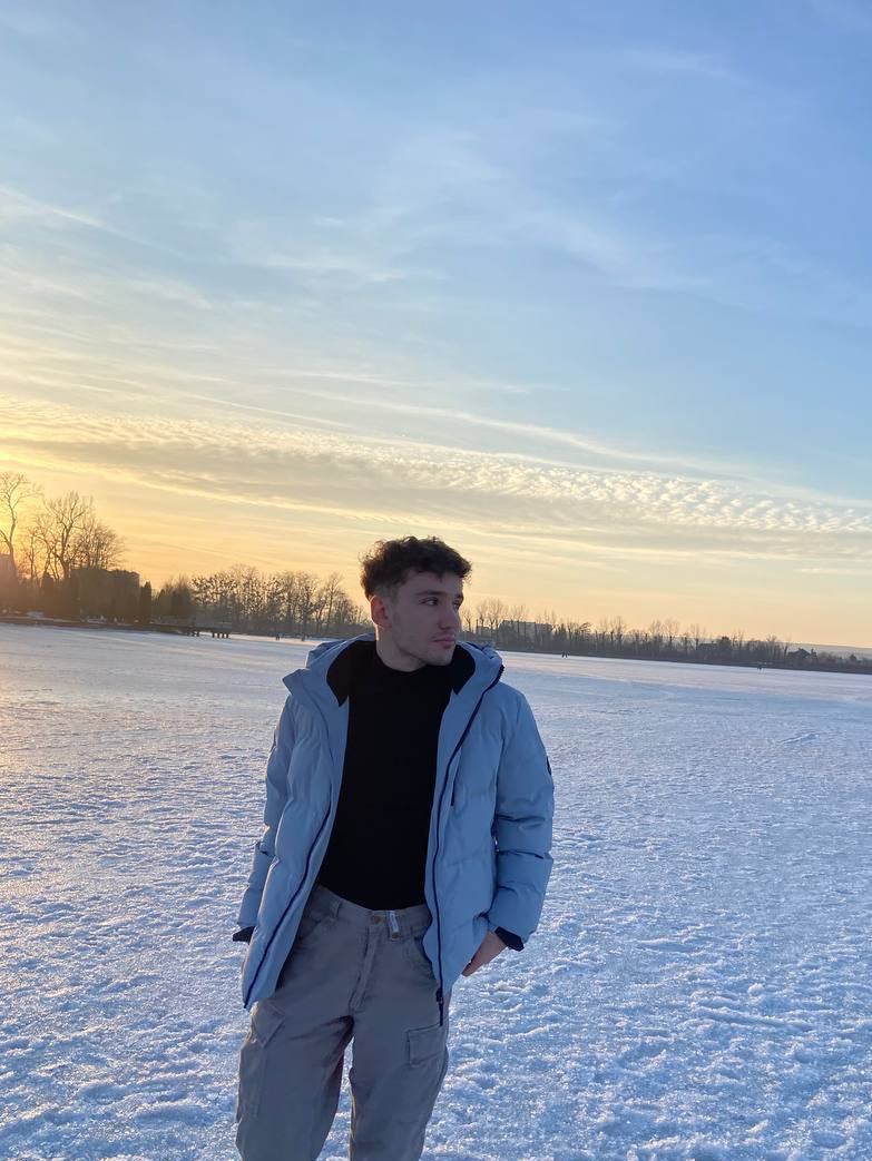 Ryan Mitchell standing on a snow-covered field with a blue sky and sunset in the background