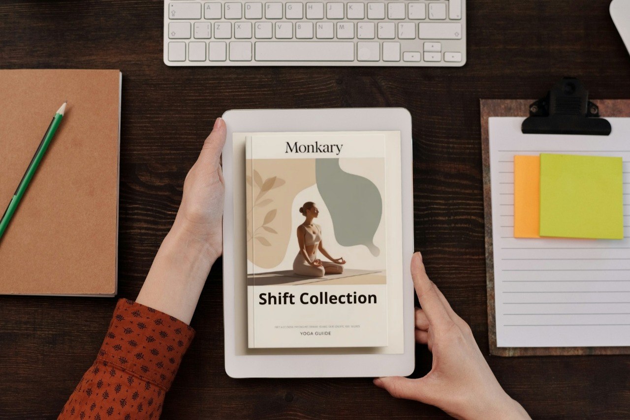 Person holding a tablet with 'Monkary Shift Collection' on a desk with a keyboard, notebook, and post-it notes.